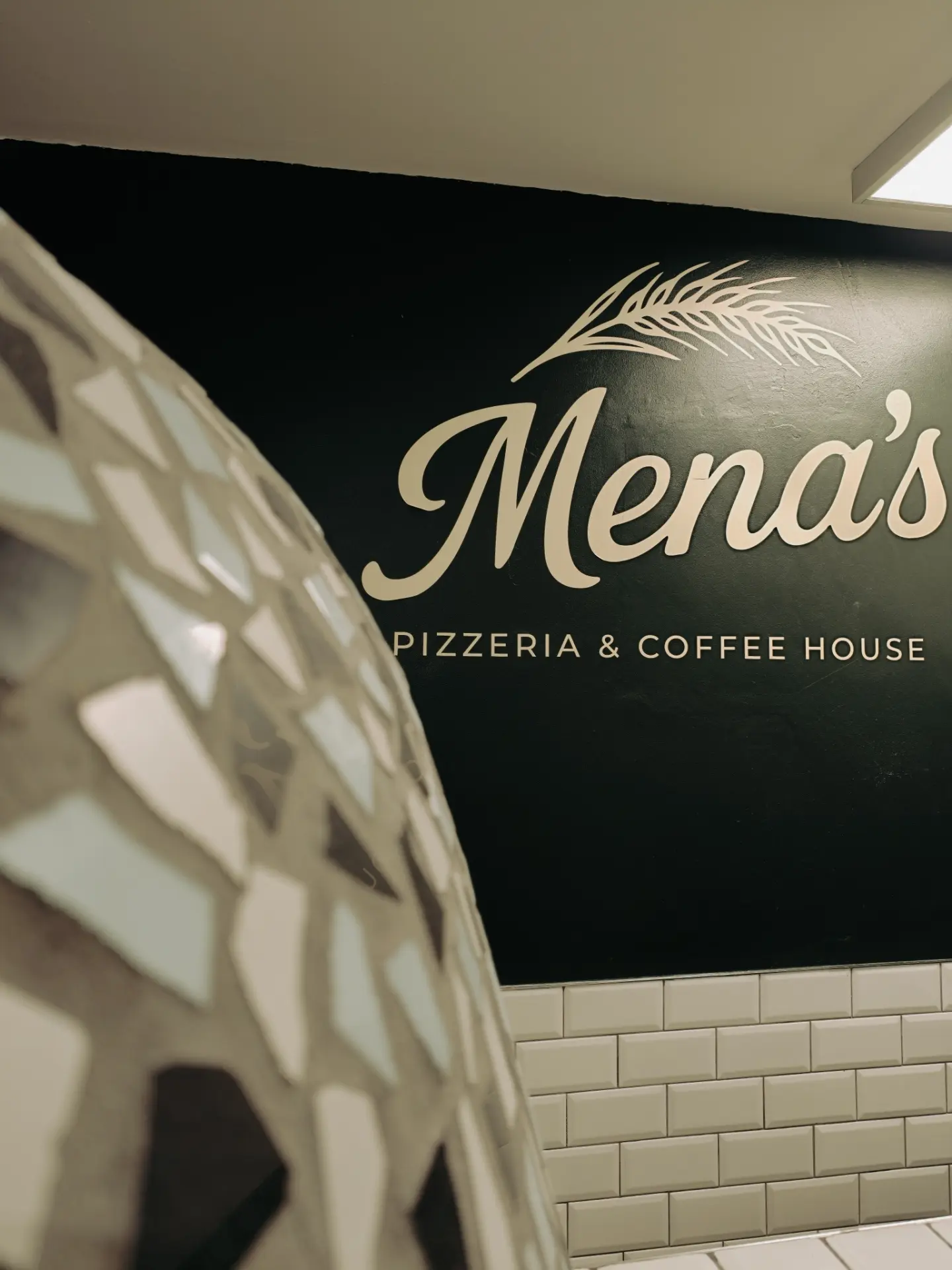 Mena’s brand wall beside the tiled pizza oven