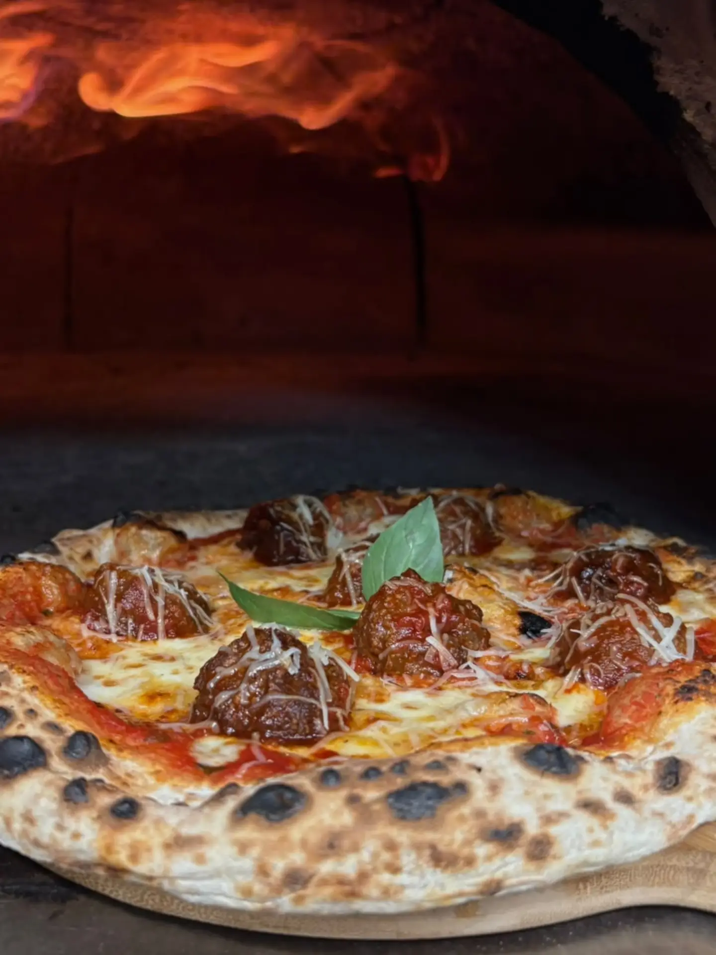 A freshly cooked Mena’s pizza at the mouth of the wood-fired oven