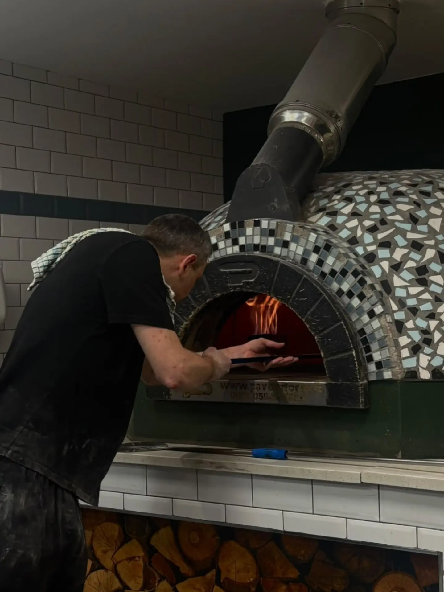 A Mena’s pizza maker tending a pizza in the wood-fired oven