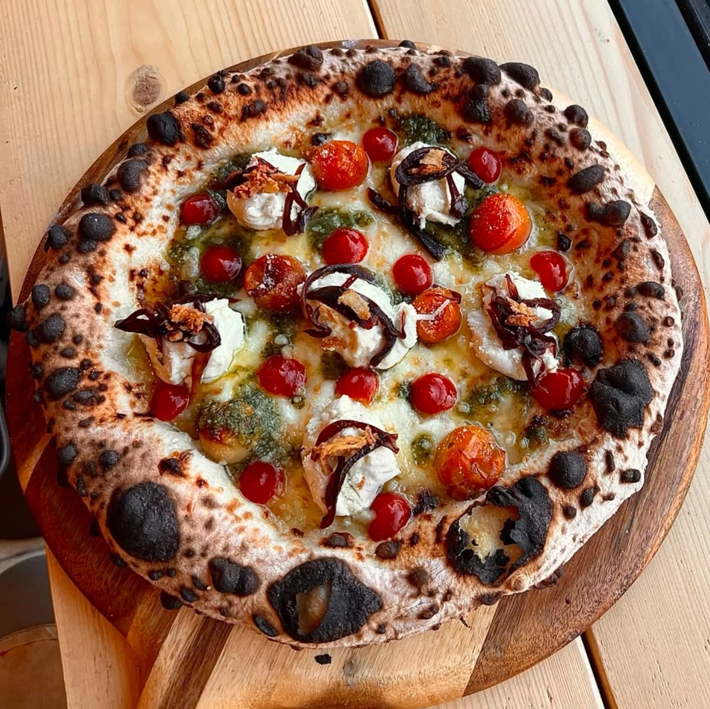 Overhead view of a wood-fired Mena’s pizza on a wooden board
